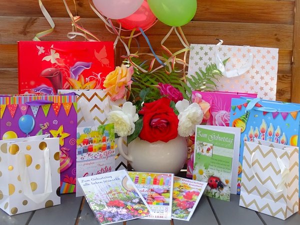 Geschenktüten und Geburtstagskarten auf einem Tisch mit Blumen, Luftballons