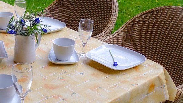 Gartentisch zum Kaffee gedeckt im blühenden Garten mit einer schönen Wachstuch Tischdecke aus dem Haushaltswarenland